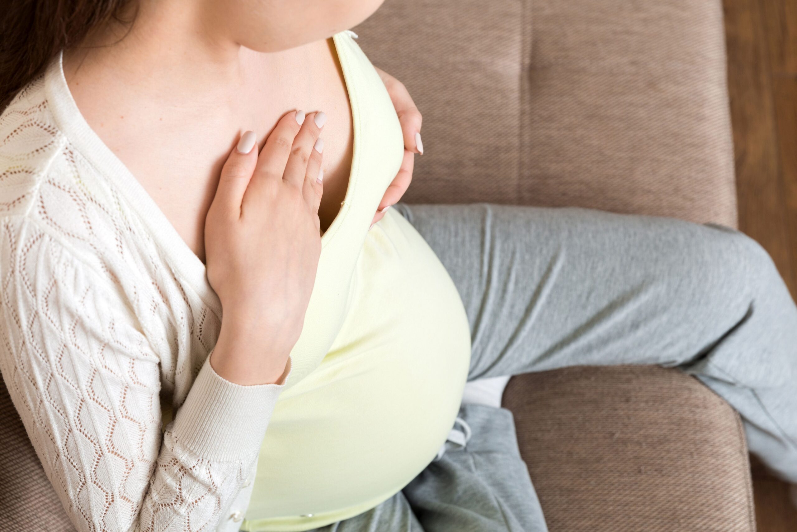 Kobieta w ciąży siedząca na kanapie cierpiąca na ból sutków