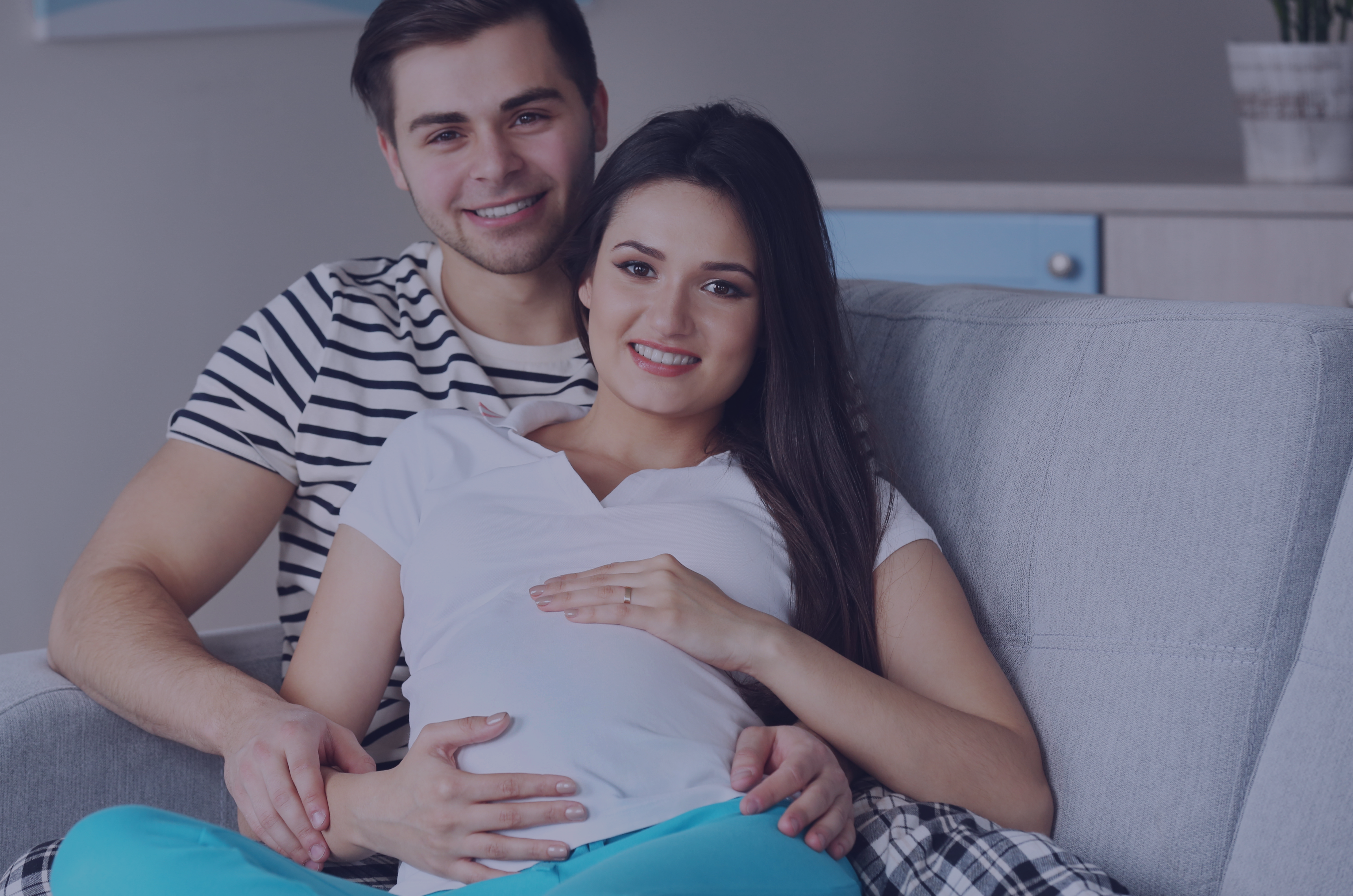 Uśmiechnięta para w ciąży siedząca na kanapie